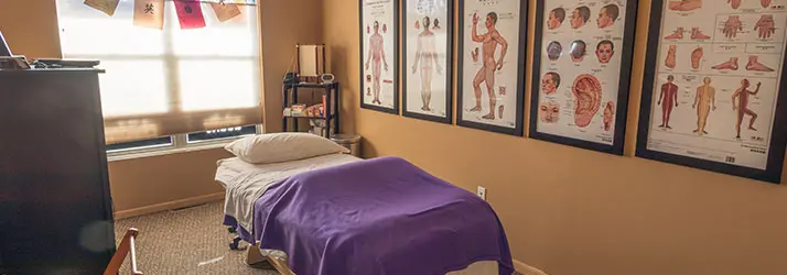 Accupuncture treatment room with purple blanket and anatomical charts at Cram Chiropractic & Wellness Center